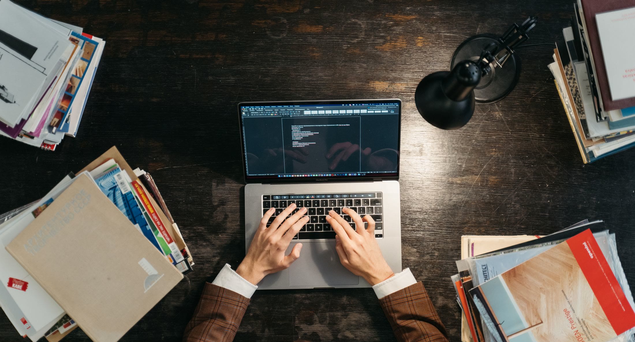 A person entering information on a laptop between stacks of filing documents
